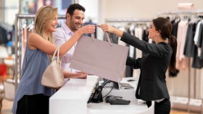 A couple standing at a counter in a large retail store taking a bag being handed to them by a sales assistant