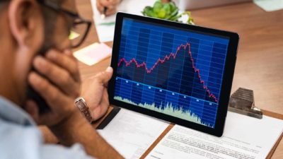 person watching share price fall on device with head resting on hand