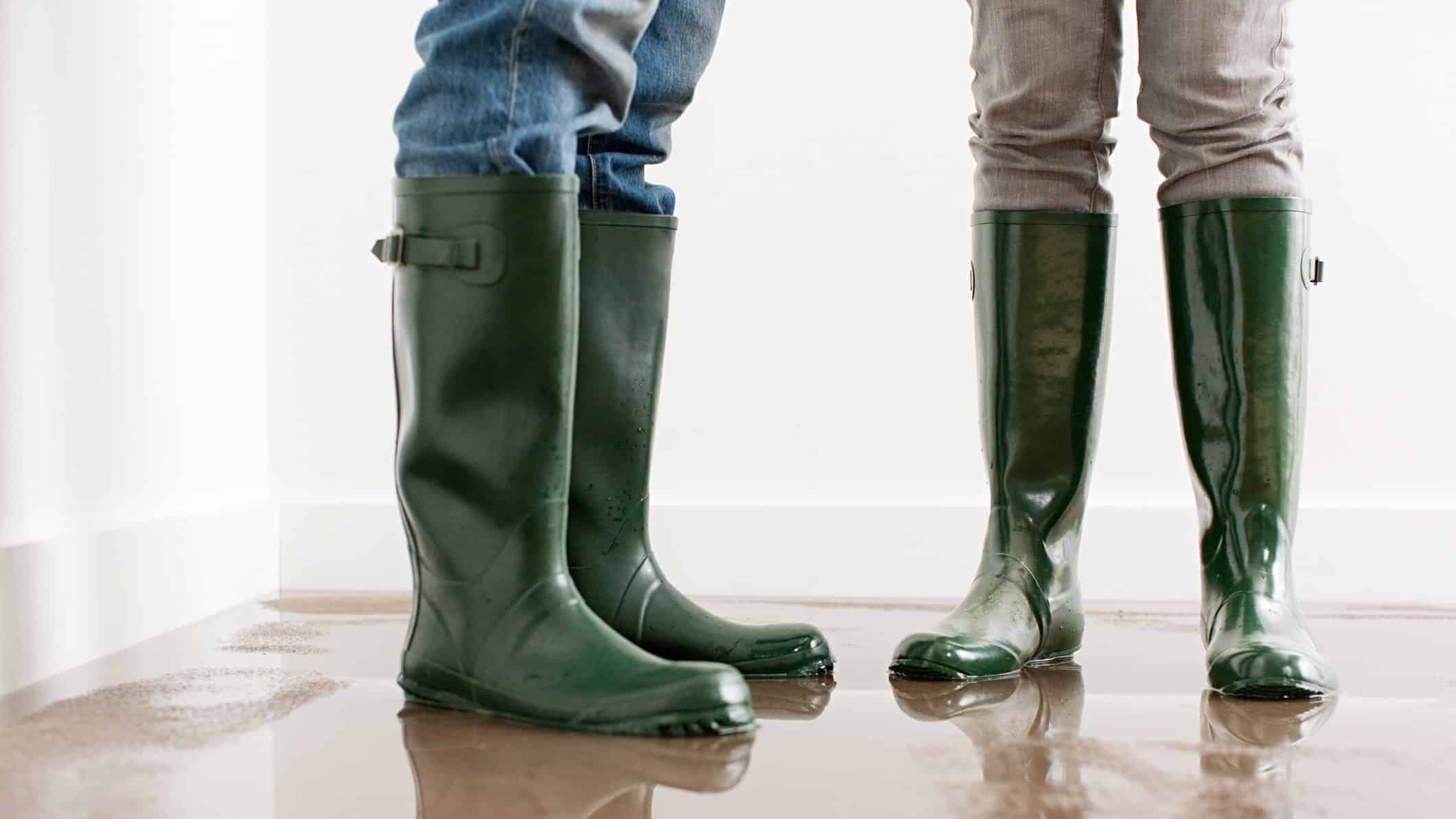 Legs and feet of two people wearing green gumboots standing in a flooded room ready to clean up.
