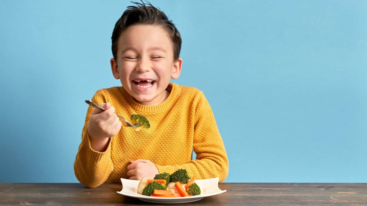 happy child eating healthy food from a bowl with fork in hand