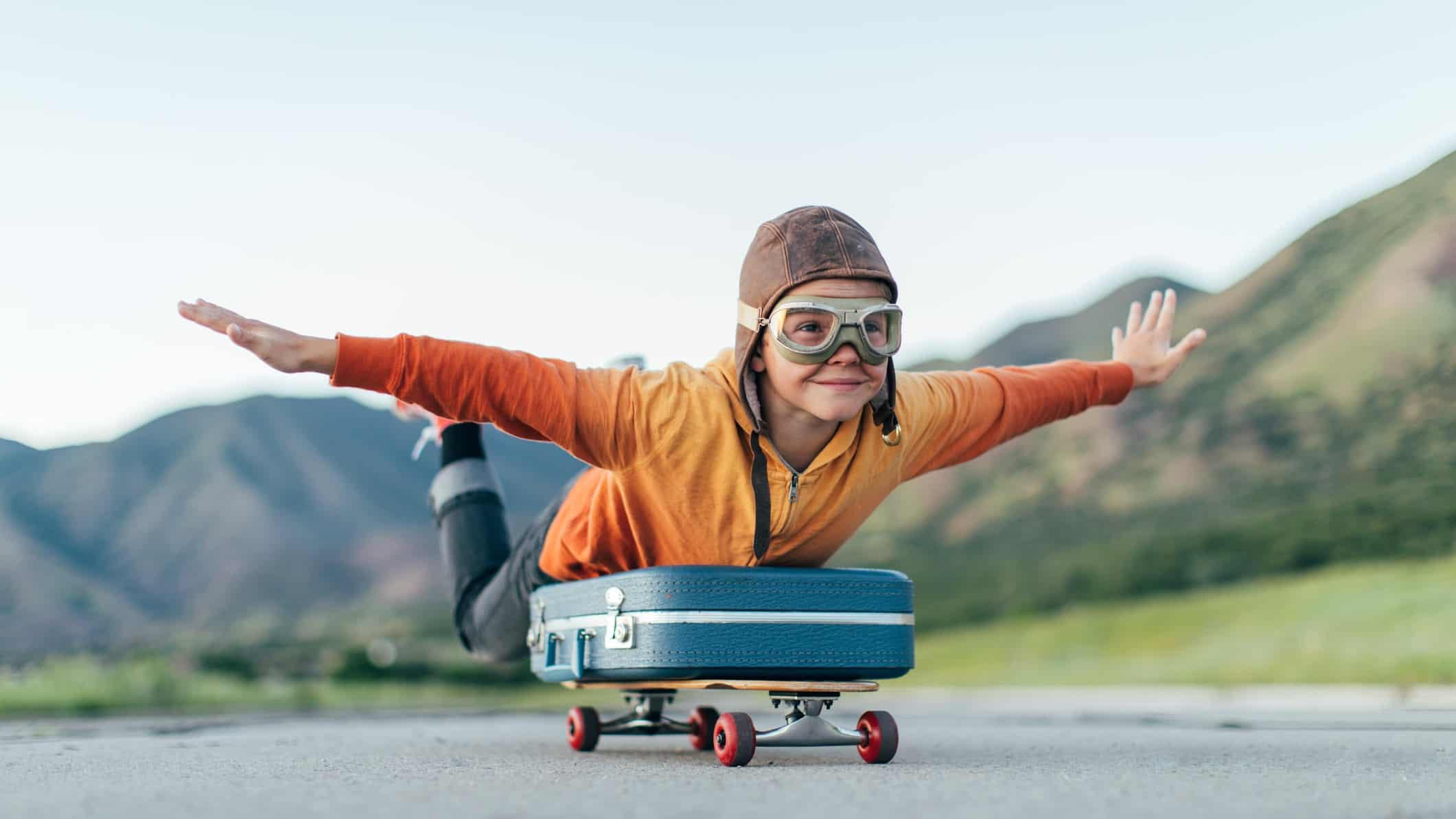 boy in flying gear simulating taking off in an aircraft by laying an a skateboard with arms out