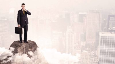 person standing tall on a mountain peak above city scene