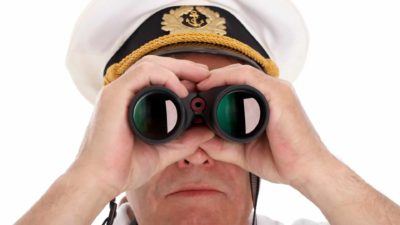 A ship captain looking through a pair of binoculars.