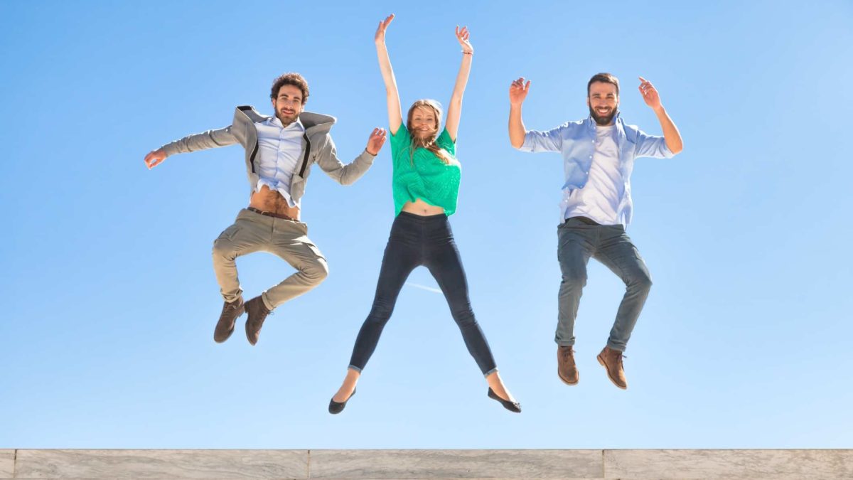 Three people leaping in celebration against a blue sky.