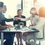 Jumbo Interactive staffers shaking hands around table agreeing to an acquisition