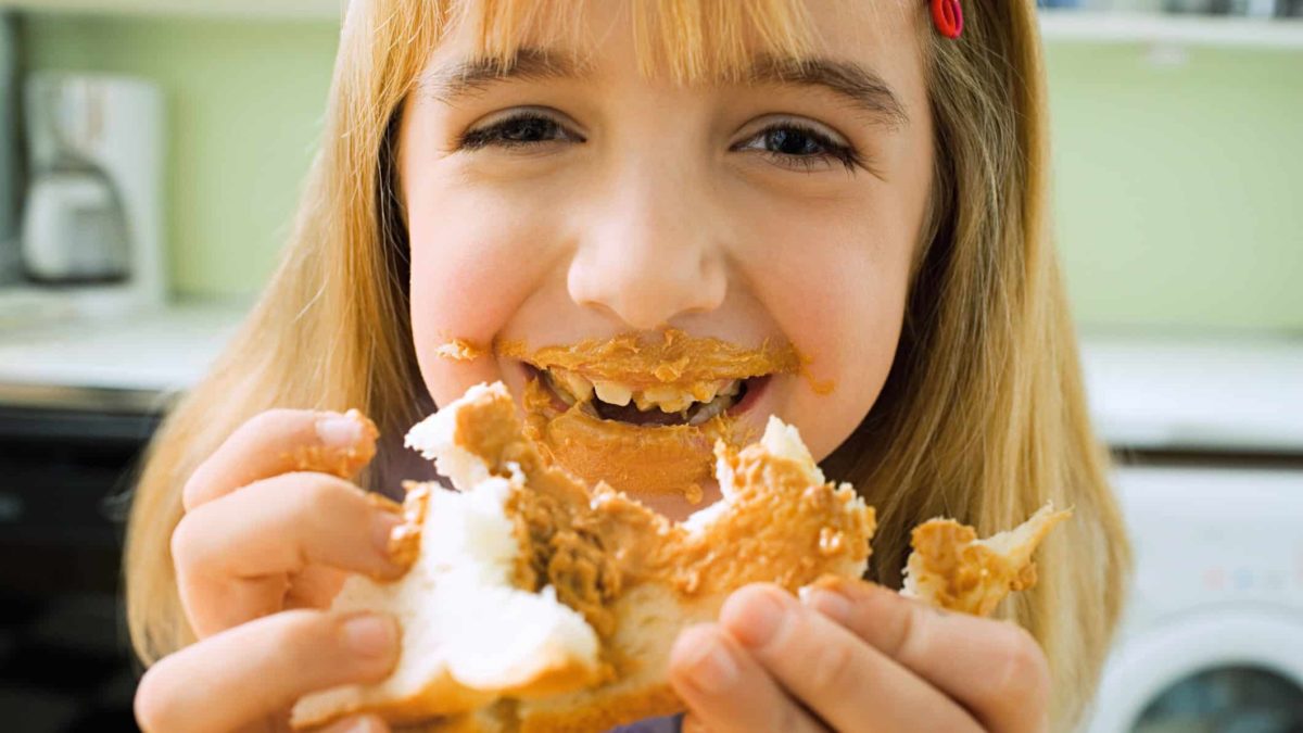girl eating peanut butter on bread with peanut butter smeared face