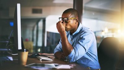 An unhappy investor holding his eyes while watching a falling ASX share price on a computer screen.