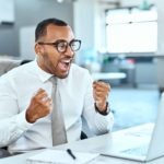 A happy person clenching fists in celebration sitting at computer.