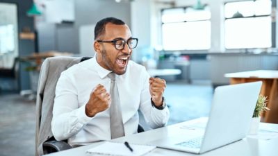 A happy person clenching fists in celebration sitting at computer.