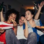 two women and a man eating pizza at a party