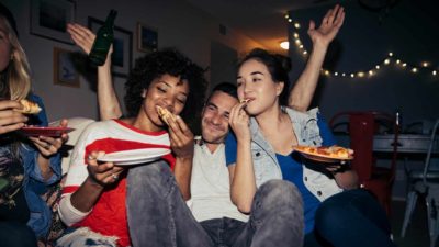two women and a man eating pizza at a party