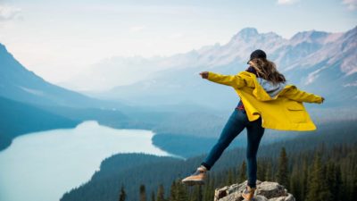 Woman standing with one leg on top a mountain looking over a lake