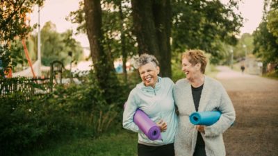 Two older women with yoga mats laughing and walking.