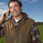 A farmer stands in a field using his mobile phone