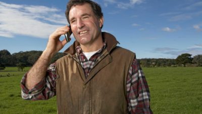 A farmer stands in a field using his mobile phone