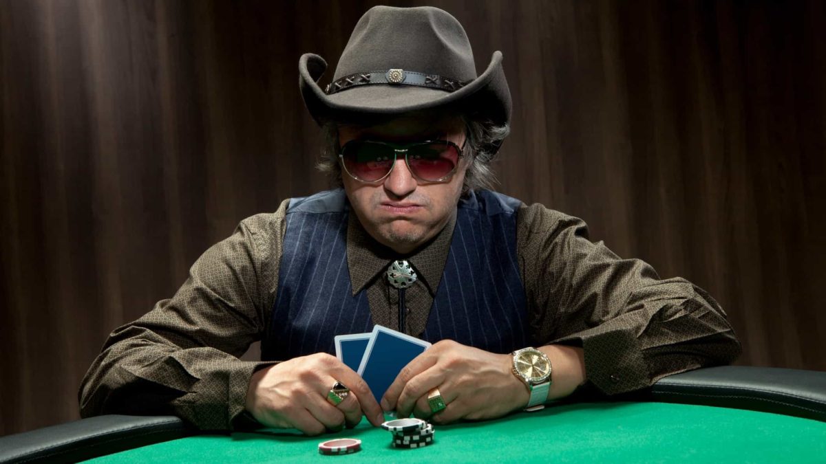Man in hat at casino table with cards and chips looking disappointed