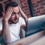 Man looking concerned head in hands at laptop
