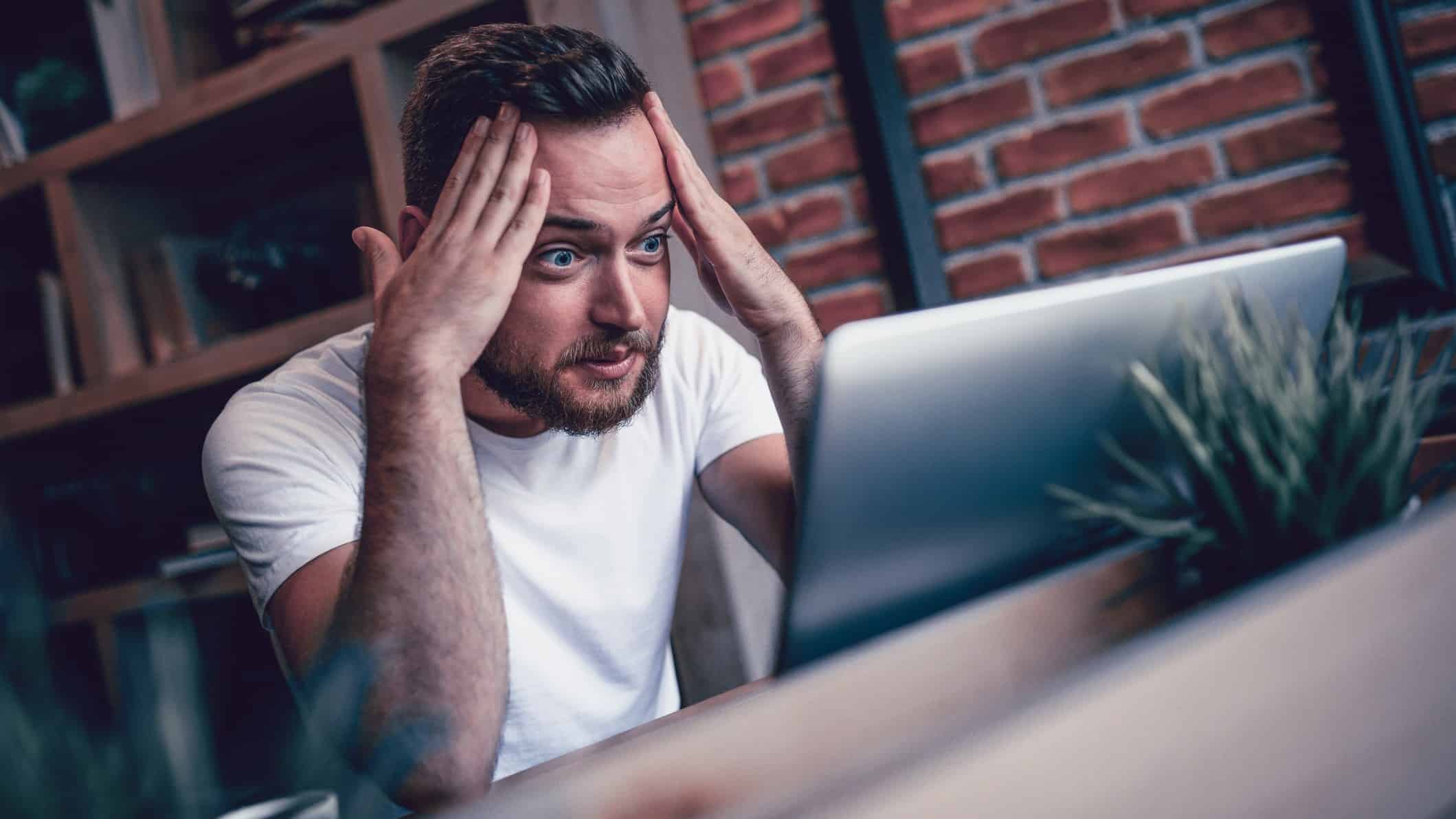 Man looking concerned head in hands at laptop