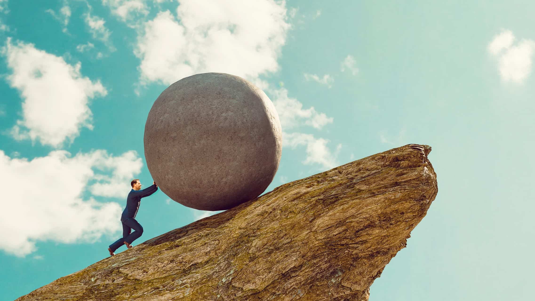 person in business suit pushing a large rock uphill