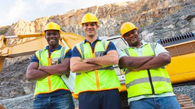 Three happy miners standing with arms crossed at a quarry.