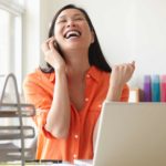 Woman on phone cheering while sitting at computer