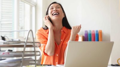 Woman on phone cheering while sitting at computer