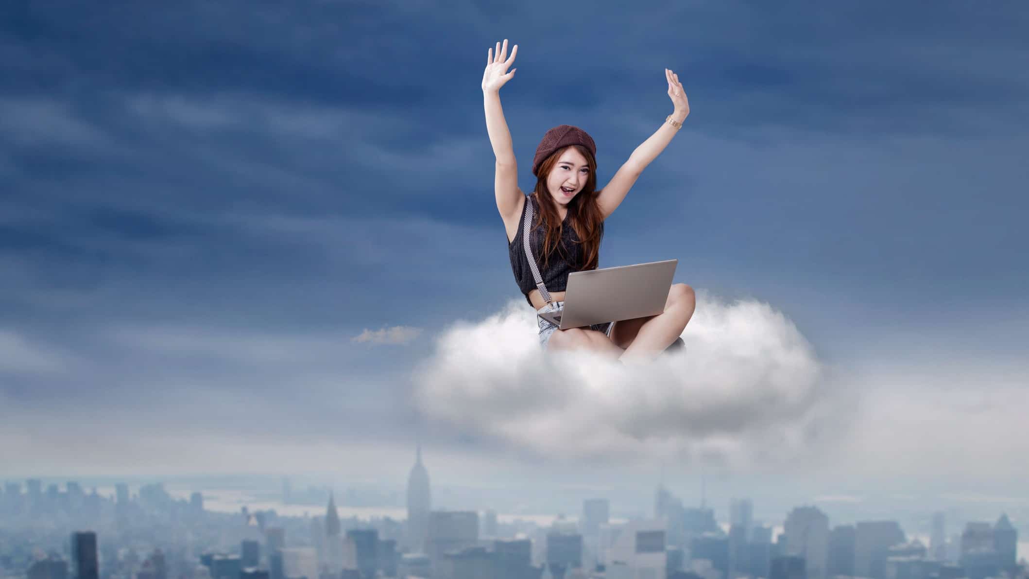 Woman using laptop sitting in cloud cheering