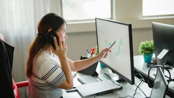 woman talking on the phone and giving financial advice whilst analysing the stock market on the computer with a pen