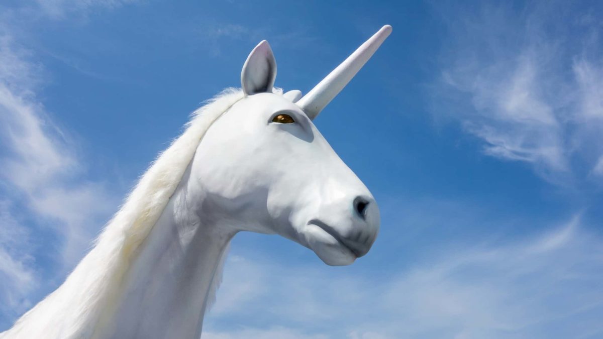 Head shot of a white unicorn against a clear blue sky.