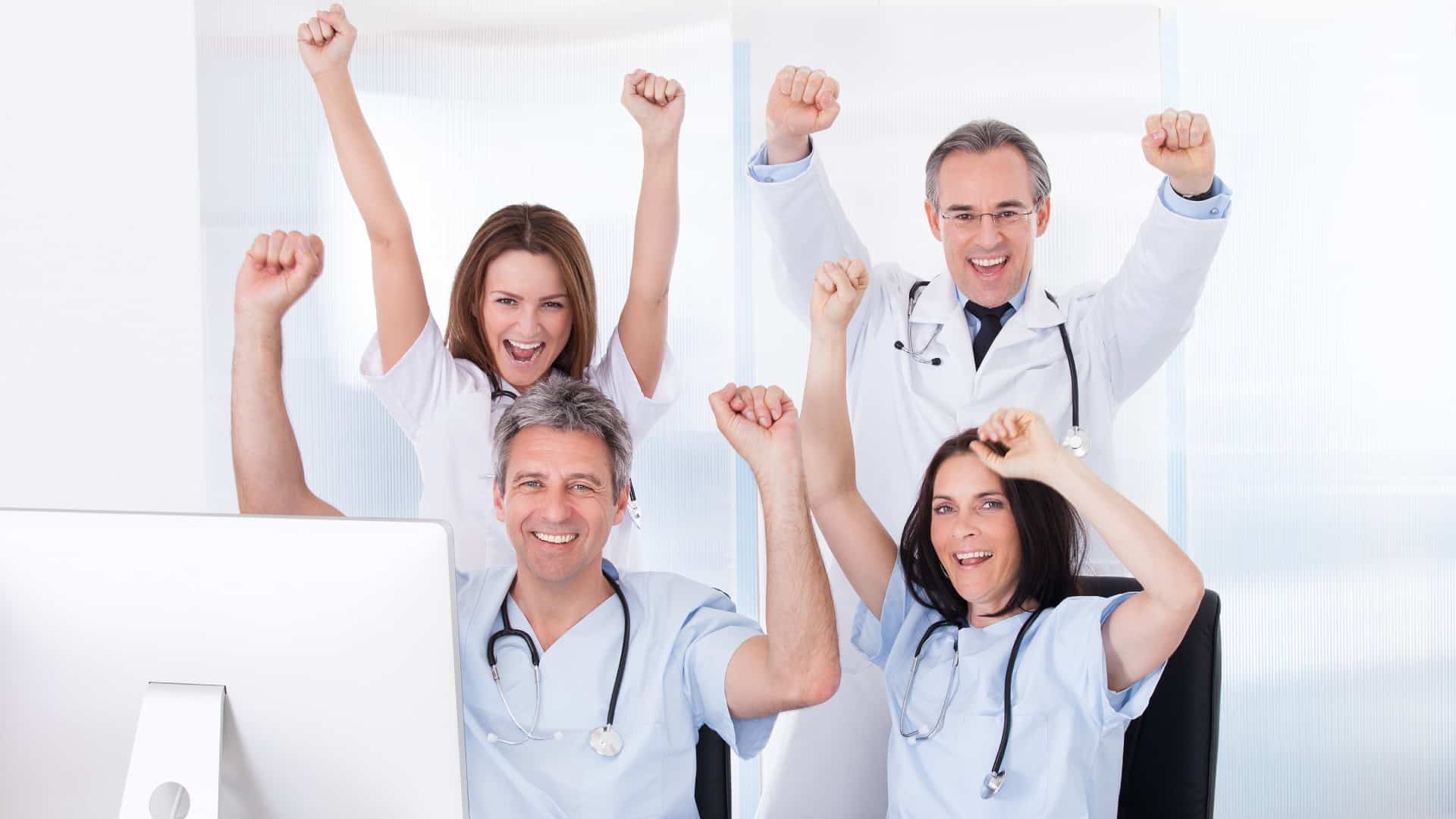 four excited doctors with their hands in the air