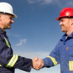 Two miners wearing hard hats shake hands over a business deal.