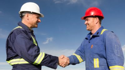 Two miners wearing hard harts shake hands over a business deal, representing the news announced today that Worley has won a contract from Santos