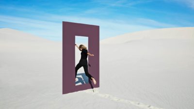 a woman jumping through a window of opportunity in sand dunes