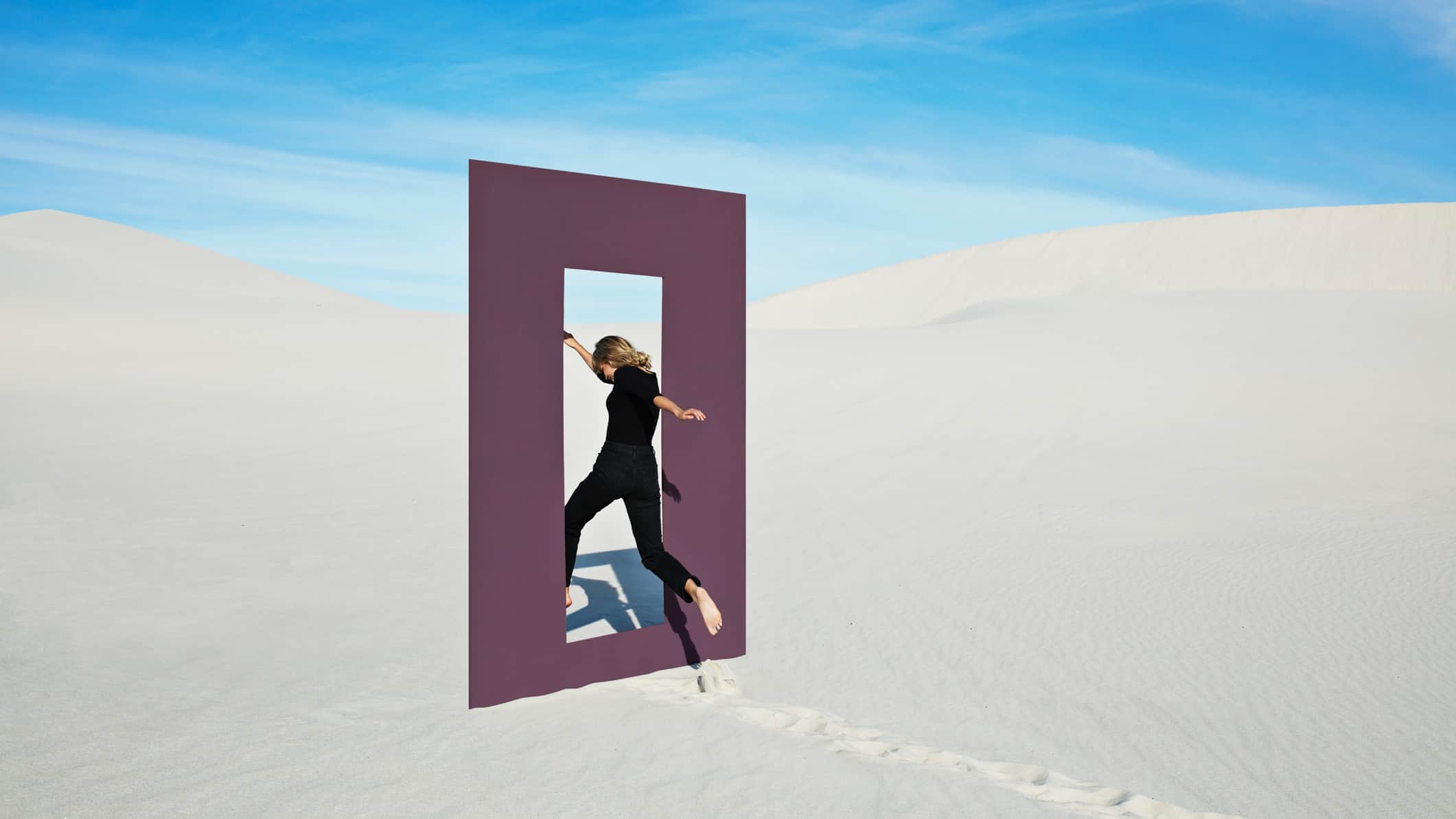 a woman jumping through a window of opportunity in sand dunes