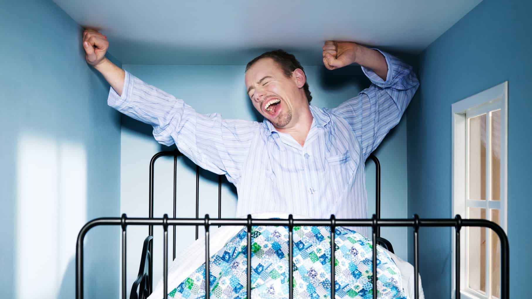 man waking up in bed in a tiny room next to a small window