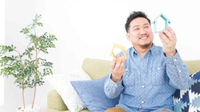 A man looking happy while holding up two little wooden houses.