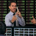 busy trader on the phone in front of board depicting asx share price risers and fallers