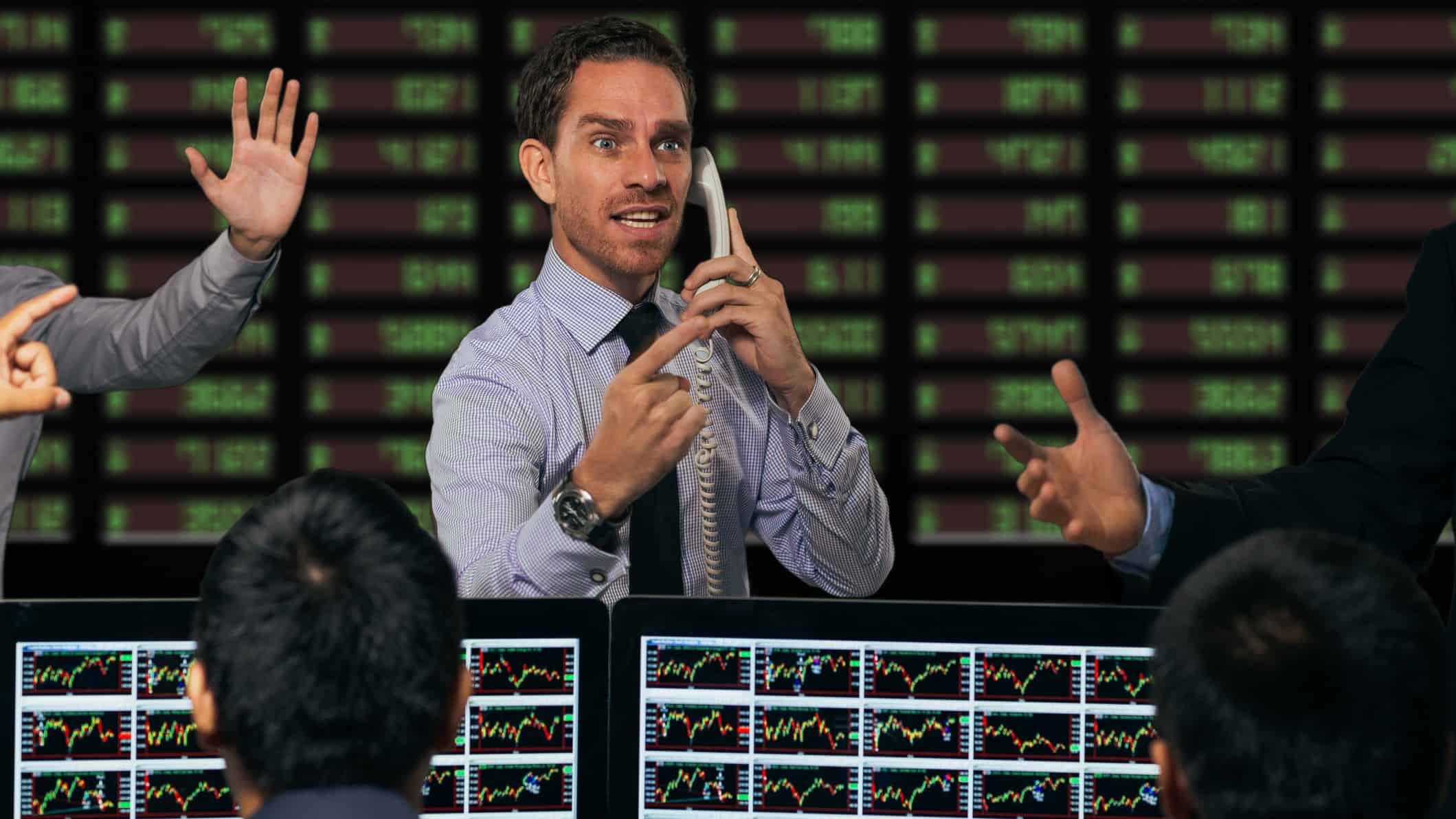 busy trader on the phone in front of board depicting asx share price risers and fallers