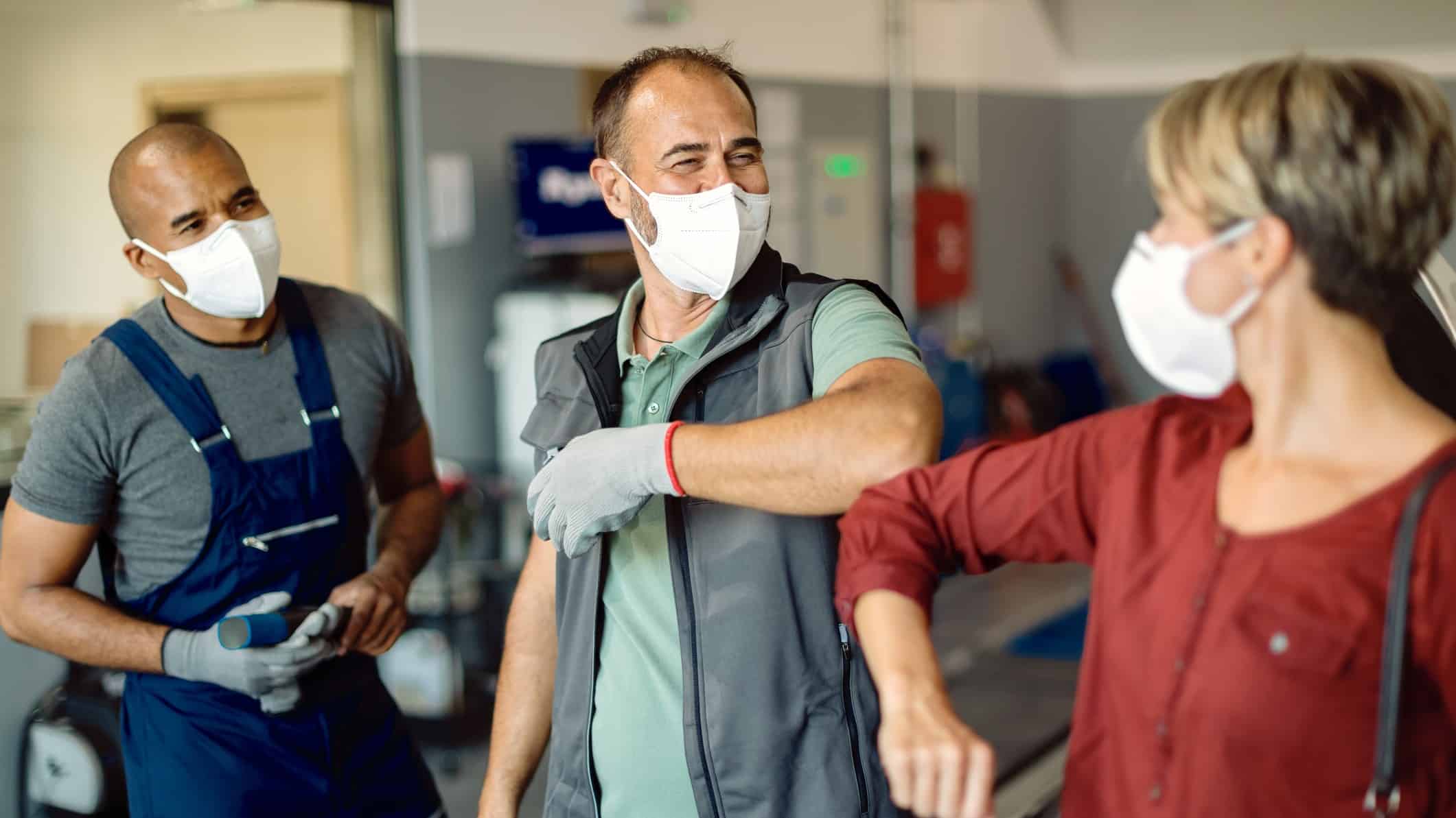 Workers wearing COVID protections mask bump elbows,indicating business still goes on