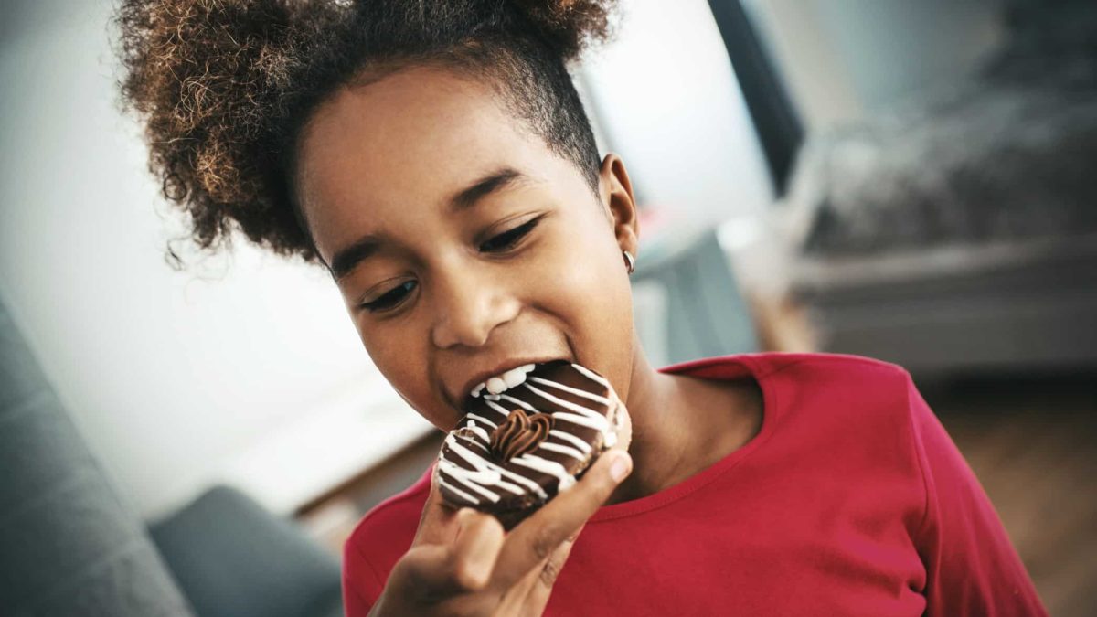 Young black girl taking a big bite out of a chocolate doughnut and she's happy about it