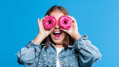 Happy woman looking through two doughnuts like binoculars