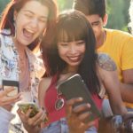 happy friends playing on phones in park