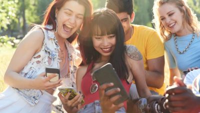 happy friends playing on phones in park