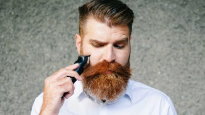 Man with beard using trimmer and looking down