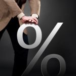 A businessman pushes a giant percentage sign down, indicating eforts to keep inflation in check
