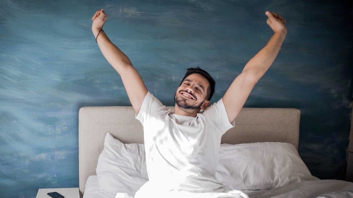 A man wakes up happy with a smile on his face and arms outstretched.