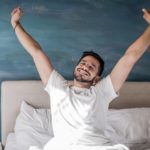 A man wakes up happy with a smile on his face and arms outstretched.