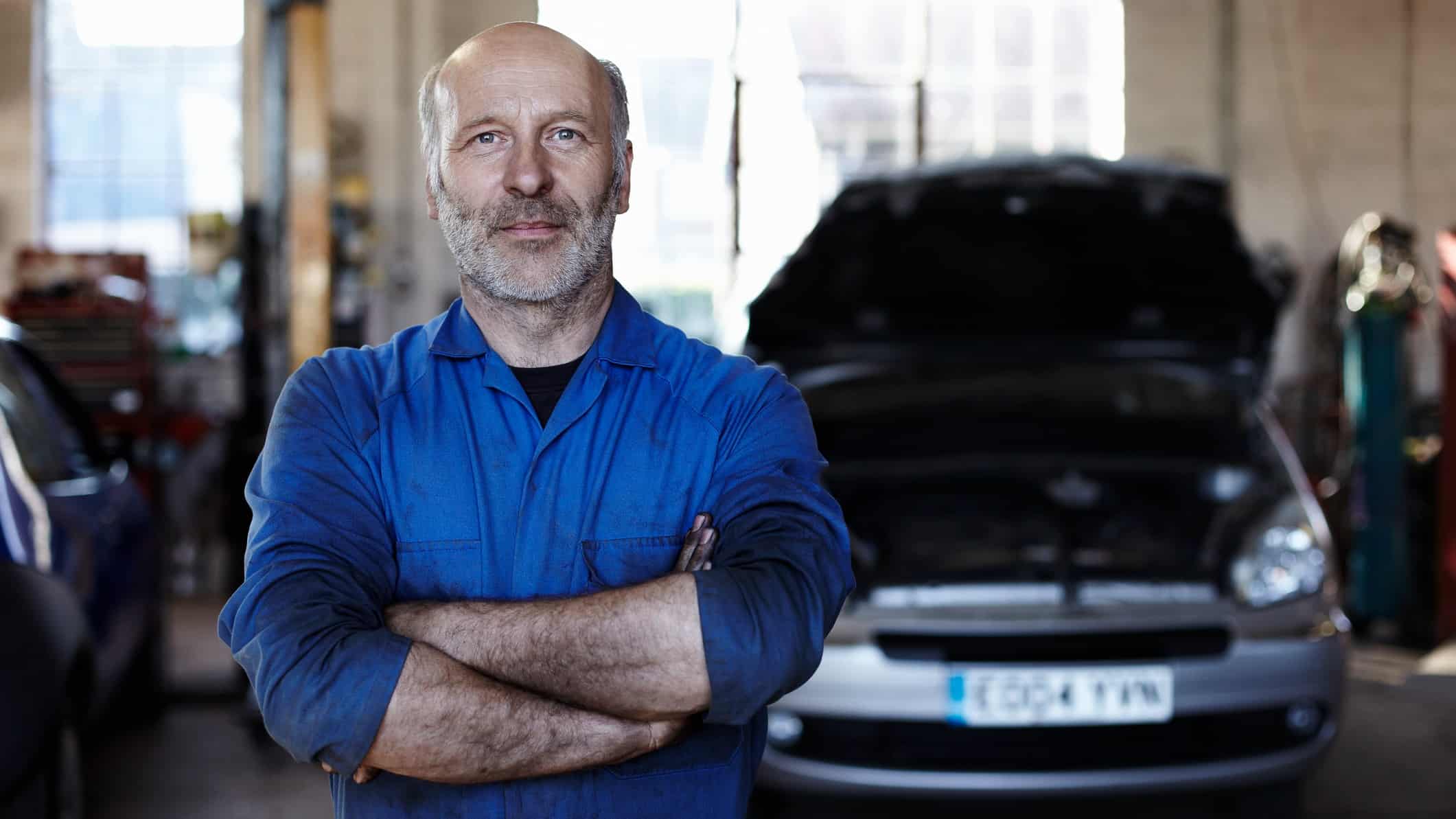 A satisfied mechanic stands next to a car in a service centre