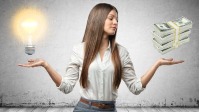 A woman holds a lightbulb in one hand and a wad of cash in the other