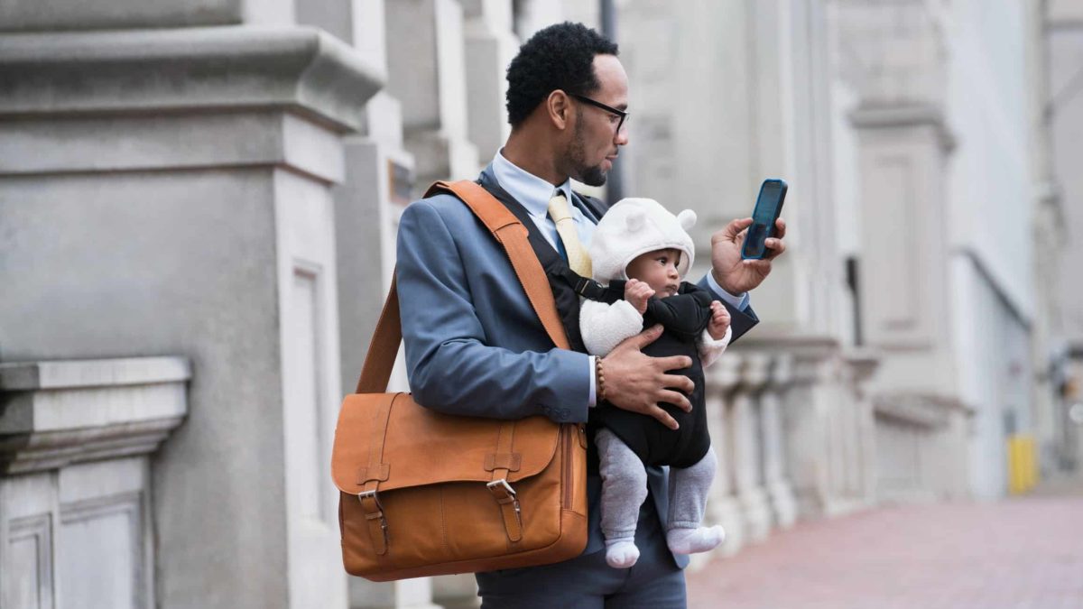 A man in a business suit holding a baby conducts a task on his phone